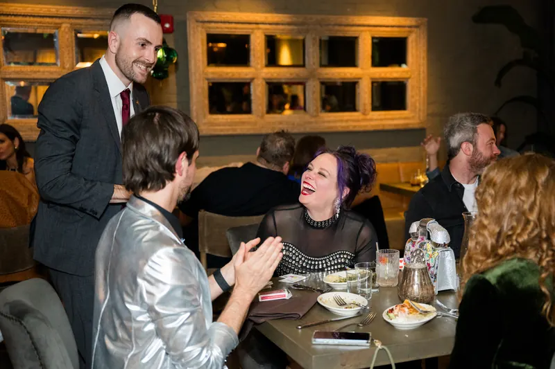 Guests laughing during a close-up magic performance at a milestone birthday party