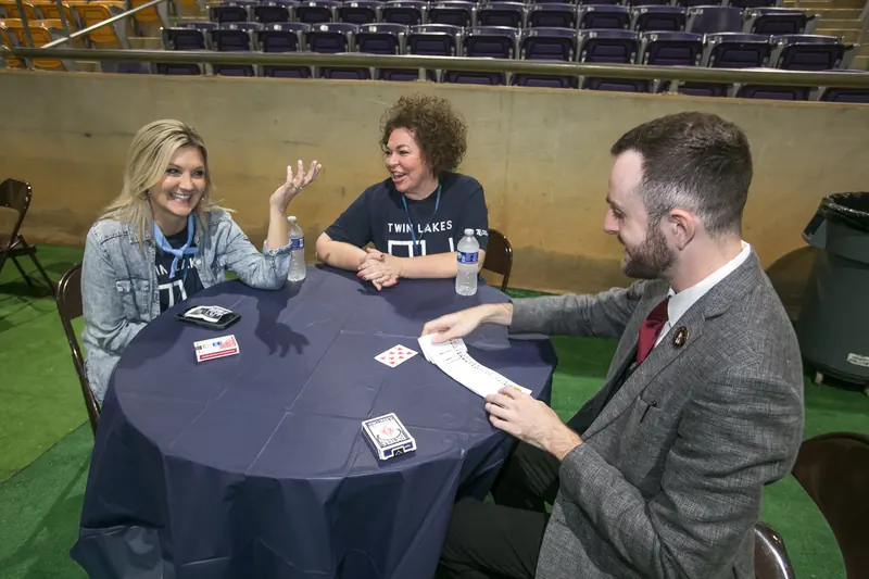 Close-up magician performing cards at a trade show table for two attendees