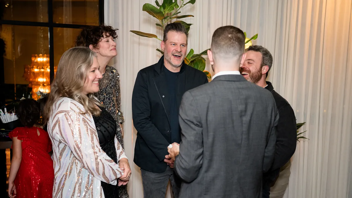 A group of guests laughing together around a close-up magic performance at an evening event