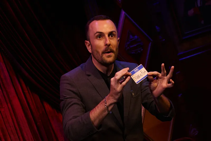 Frankie Foti performing on stage, holding up a signed name badge