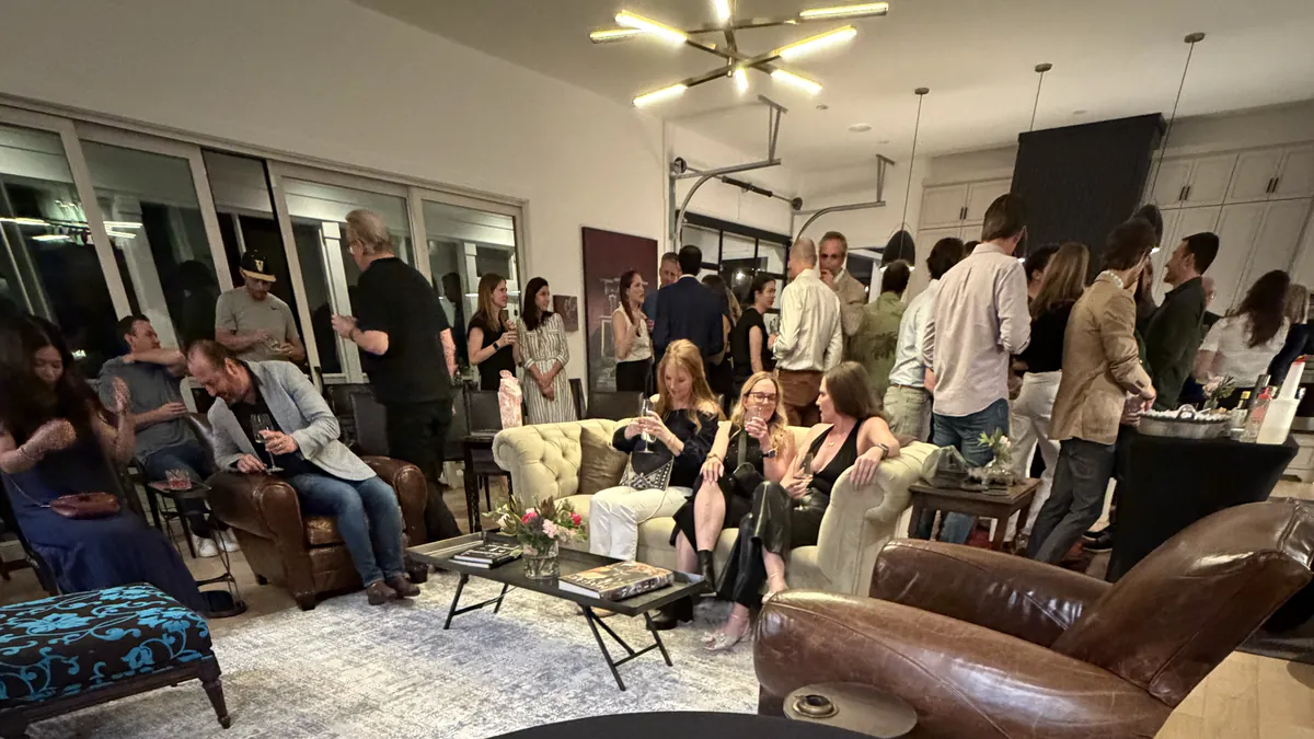 Guests mingling with drinks in a living room at a private house party, with the magician&rsquo;s close-up table in the foreground