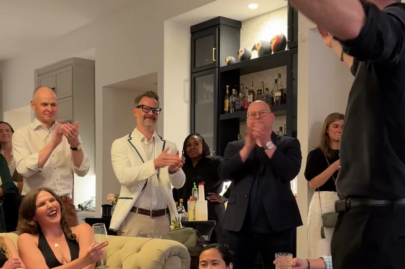 Guests seated and standing in a living room applauding during Frankie Foti&rsquo;s parlour magic show